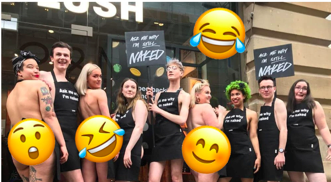 Photo of LUSH staff, most of whom are women, wearing only an apron and standing outside the store.