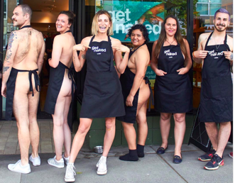 Photo of LUSH staff, most of whom are women, wearing only an apron and standing outside the store.